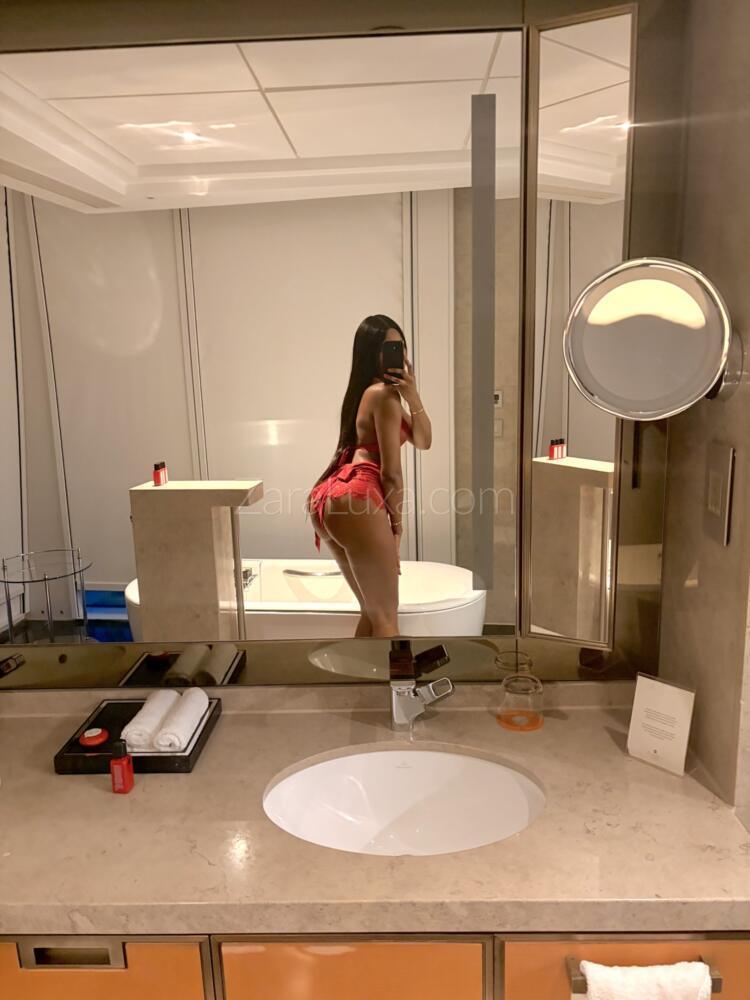 Zara Luxa taking a mirror selfie posing slightly bent forward showing off her amazing bum in a red thong