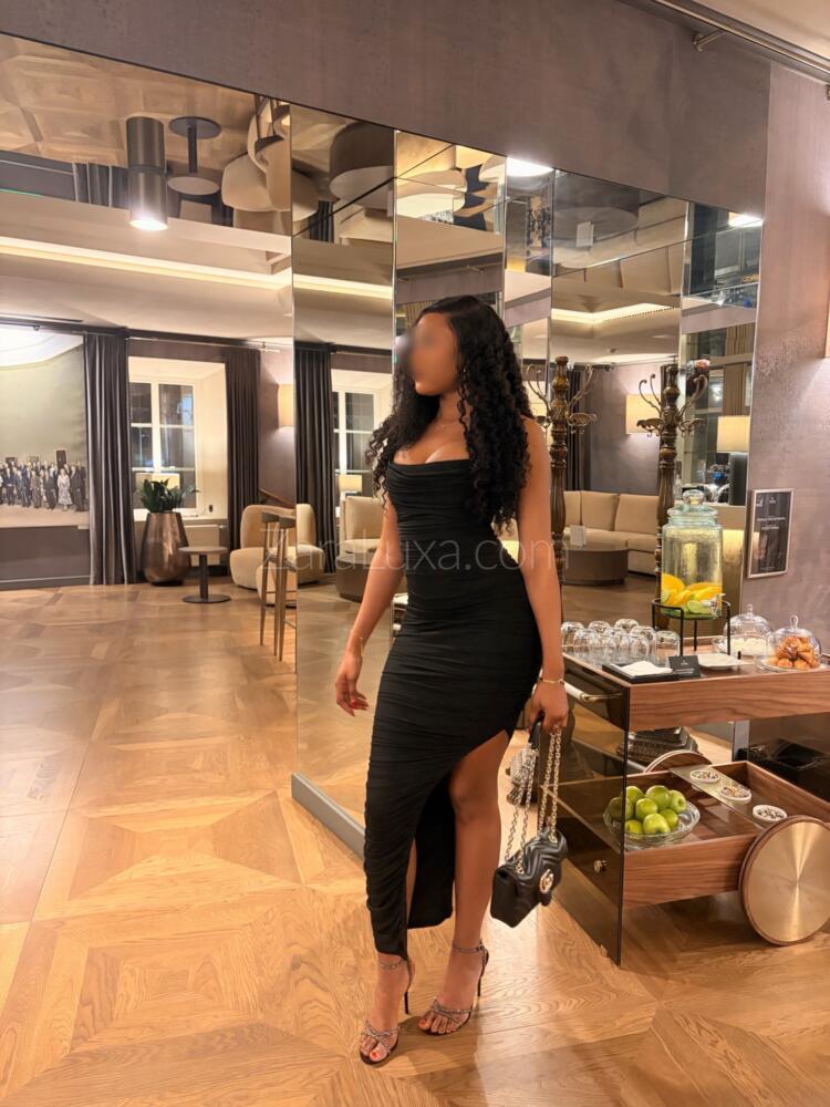 High class London escort Zara Luxa wearing a long tight black dress in a hotel lobby