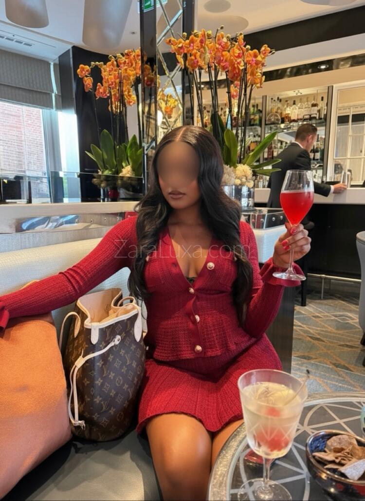 Zara Luxa wearing a burgundy suit dress whilst sat at a bar holding a glass of red wine