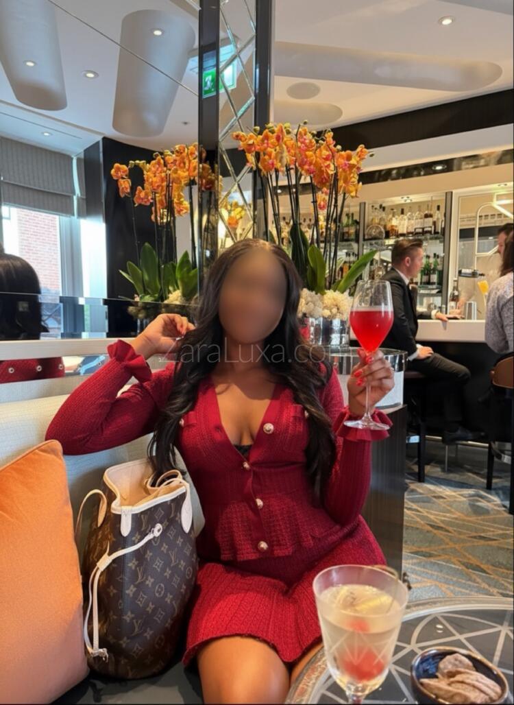 Zara Luxa enjoying a glass of red wine at a bar wearing a burgundy suit set