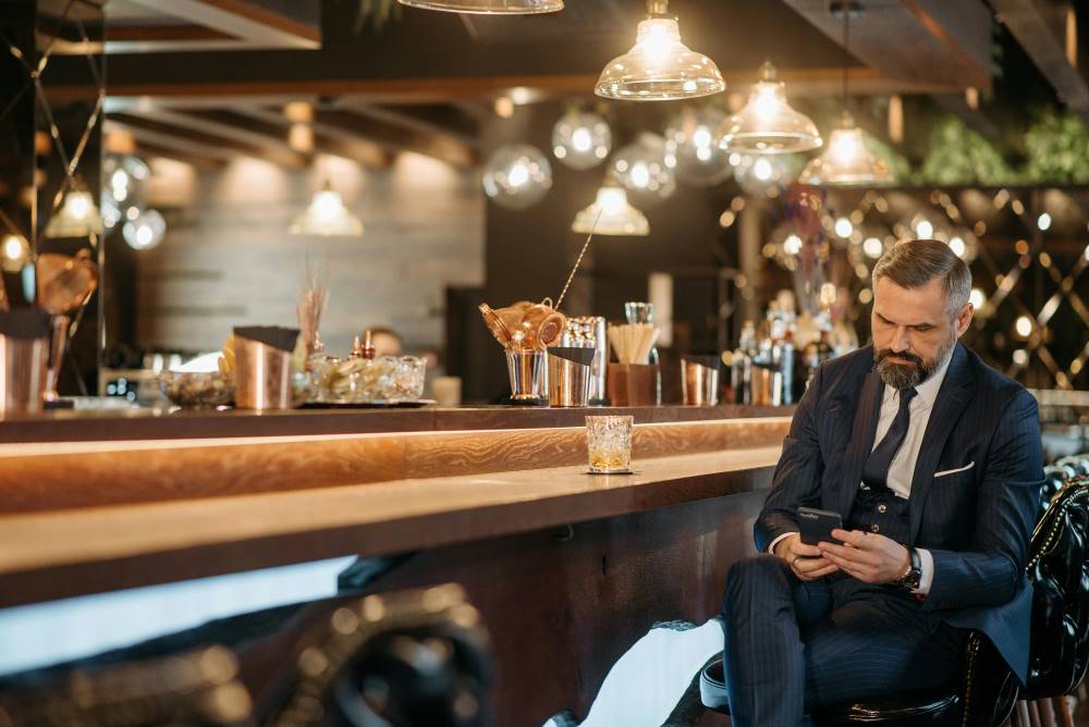 A man in suit sitting at a bar on his phone