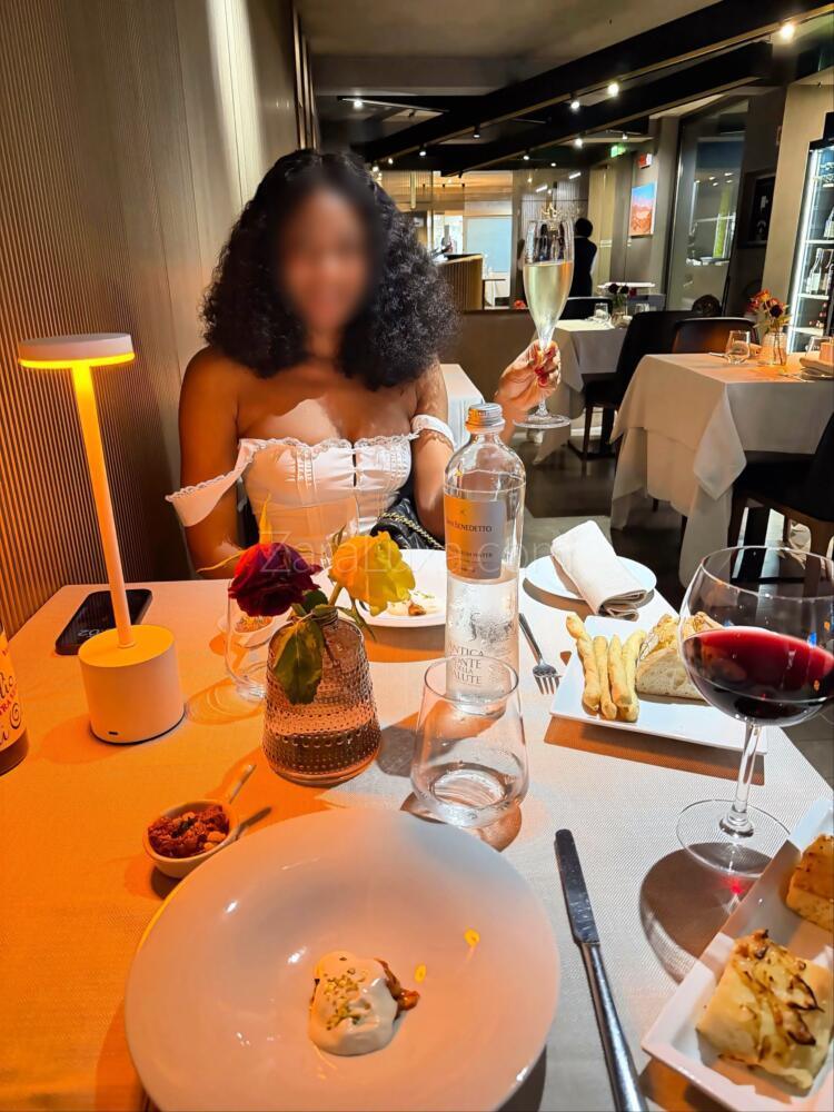 Zara Luxa in a white off-the-shoulder dress, dining at a candlelit table in a Lake Como hotel restaurant